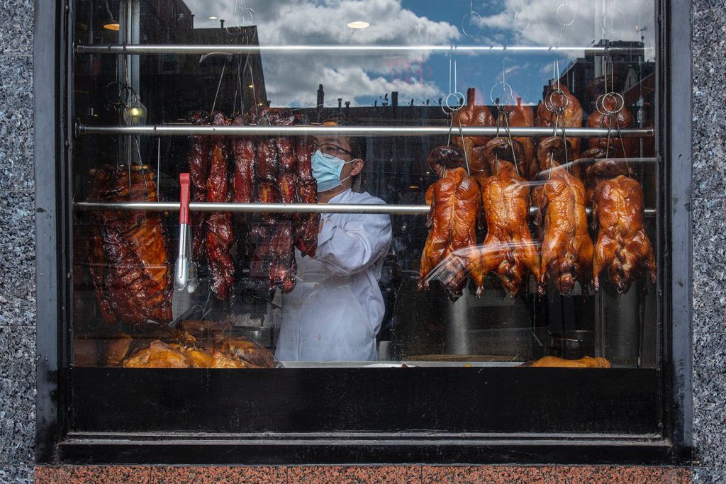 Chinese BBQ Horizontal color photograph of a worker with face mask preparing the meats in the window of a restaurant and takeout during the coronavirus pandemic in Chinatown. Boston, MA